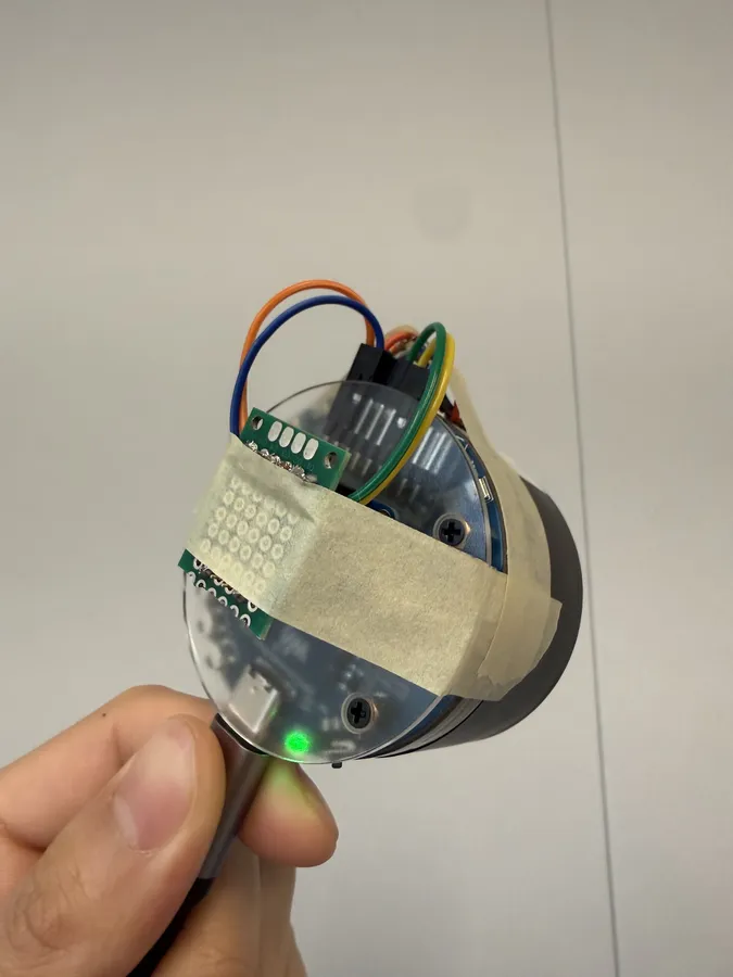 The round ESP32-S3 audio board held in a hand, with sensor wires taped to it