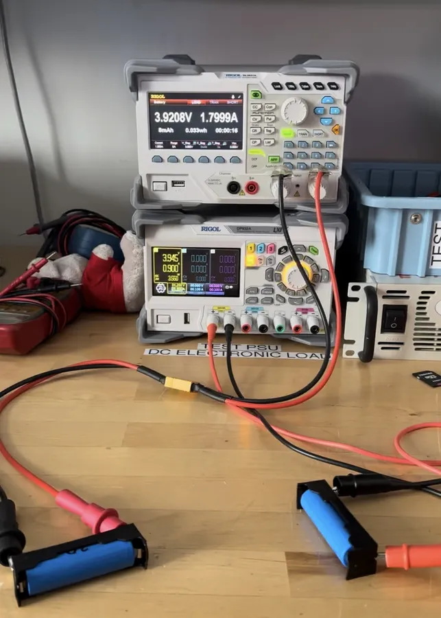 A lab bench with a DC power supply and a DC electronic load wired to 18650 cells in holders