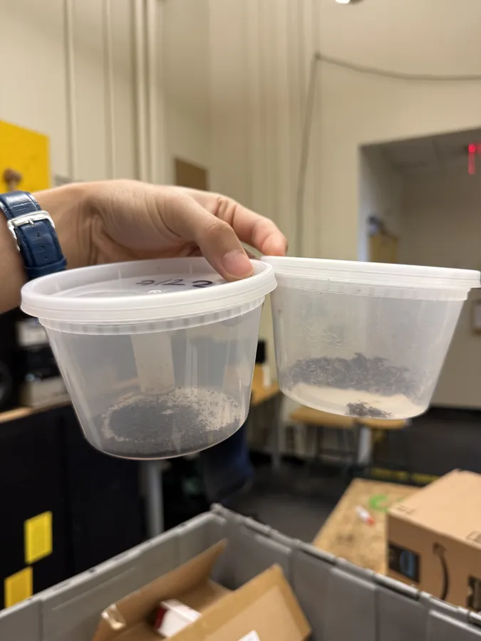 A hand holding two plastic sample cups with char from the run in the bottom