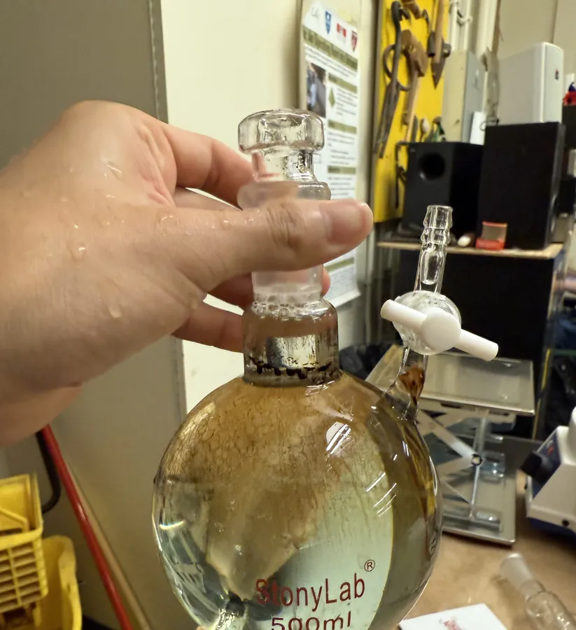 A hand holding the stoppered round-bottom flask with water inside, being cleaned after the run