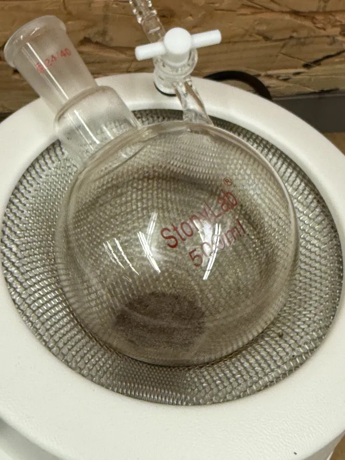 A round-bottom flask sitting in the mesh of a heating mantle, dark material in its base