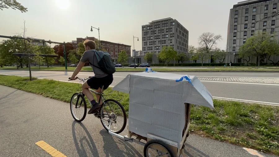 Side view of the rider towing the trailer with its white shade canopy and awnings along the river path