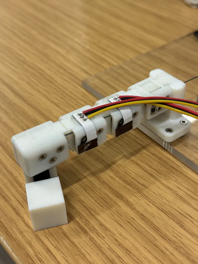 A white 3D-printed test finger on a desk, with flexible PCBs wrapped over two joints and red, yellow and black wires running to them